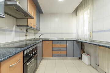 Kitchen with L-shaped base units, blue countertop and combined wood and blue doors and integrated...