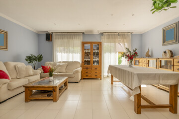 A living room with a large wooden dining table with a shelf and upholstered armchairs