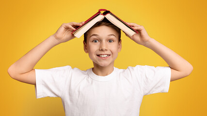 A young boy stands with a book raised above his head.