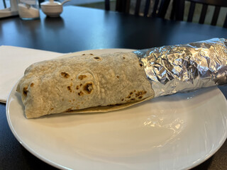 Delicious Wrapped Burrito in Foil on White Plate