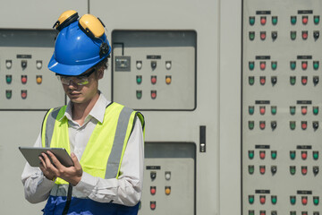 Focused young technician in safety gear inspects and controls industrial electrical equipment on a...