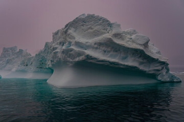 Solitary iceberg with aqua water purple skies in Greenland floating