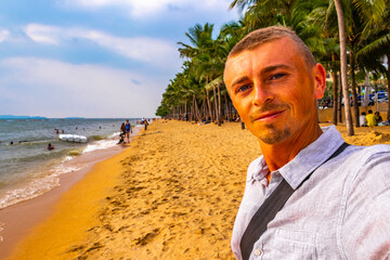 Tourist takes selfie beach waves sand people palm Pattaya Thailand.
