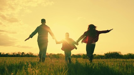 Happy family running flying holding hands at sunset sunny field back view slow motion. Mother...