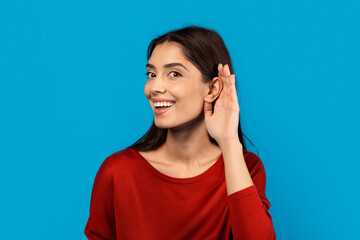 A woman with a joyful expression on her face is smiling and touching her ear with her hand, indicating she might be listening or adjusting an earpiece. She appears content and engaged in the moment.