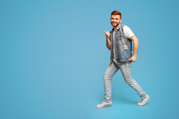 Naklejka premium Cool millennial man dancing with thumbs up gestures on blue background, studio, copy space