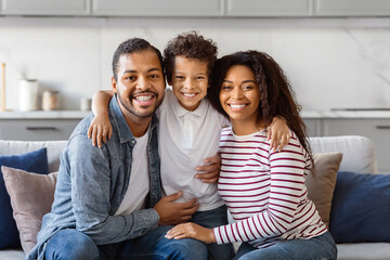 Happy African American family is seated on a comfortable couch. They seem to be engaged in...