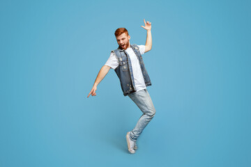 Young cheerful man dancing on tiptoes on blue studio background, copy space, full length, studio