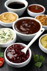 Different tasty sauces in bowls, parsley and chili pepper on black wooden table