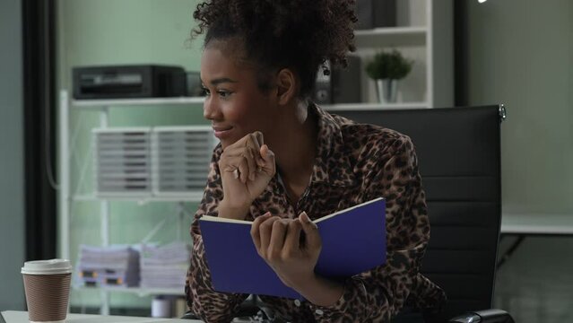 A young African American woman in a blue formal shirt with afro brown hair works as a product designer in a modern office, utilizing skills in design, CAD, CNC, and CNF.