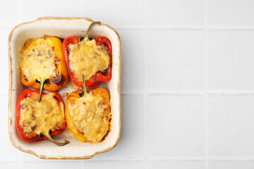 Delicious stuffed peppers in baking dish on white tiled table, top view. Space for text