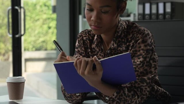 A young African American woman in a blue formal shirt with afro brown hair works as a product designer in a modern office, utilizing skills in design, CAD, CNC, and CNF.