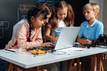 Skilled kids learning to program remote car. Schoolgirl in pink cloth use laptop for coding. Other...