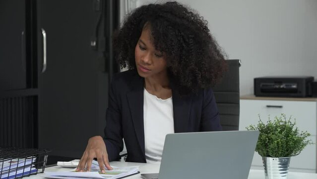 A young African American woman in a blue formal shirt with afro brown hair works as a product designer in a modern office, utilizing skills in design, CAD, CNC, and CNF.