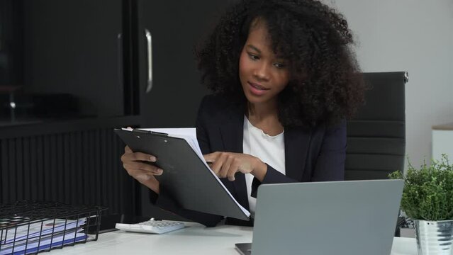 A young African American woman in a blue formal shirt with afro brown hair works as a product designer in a modern office, utilizing skills in design, CAD, CNC, and CNF.