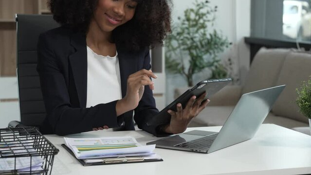 A young African American woman in a blue formal shirt with afro brown hair works as a product designer in a modern office, utilizing skills in design, CAD, CNC, and CNF.