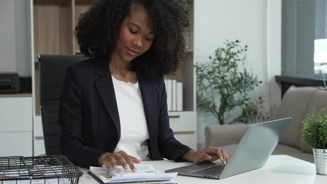A young African American woman in a blue formal shirt with afro brown hair works as a product designer in a modern office, utilizing skills in design, CAD, CNC, and CNF.