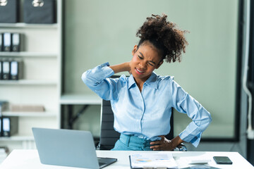 A young African American woman in a blue formal shirt with afro brown hair, suffering from office syndrome, navigates the challenges of being a businesswoman in a modern office.