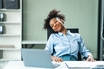 A young African American woman in a blue formal shirt with afro brown hair experiences office syndrome, tiredness, and pain from prolonged sitting in a modern office environment.