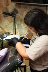Latin woman young adult tattoo artist making tattoo stencil in paper for client in a tattoo studio....
