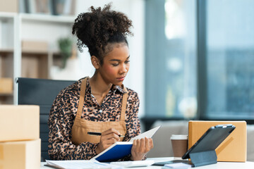 A young African American woman with afro brown hair works in a modern office, managing her small business, utilizing laptop technology for e-commerce, shipping, and marketing, sme box.