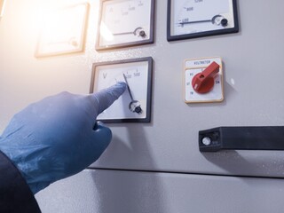 An engineer wearing blue gloves shows the working voltage value on the main control panel, the...