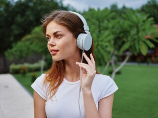 Woman portrait in headphones happiness smile in a white T-shirt listening to music and walking down the street, in front of palm trees