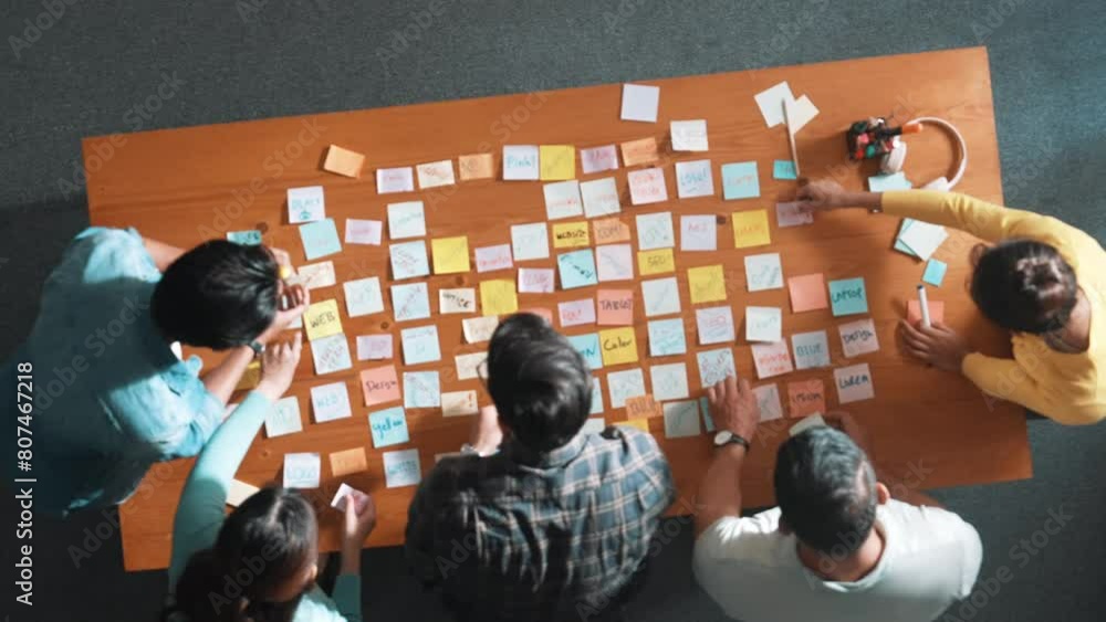 Poster top down view of smart project manager pointing at sticky note on meeting table with sticky notes. s