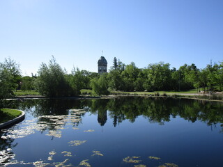 placid pond reflects trees and distant tower