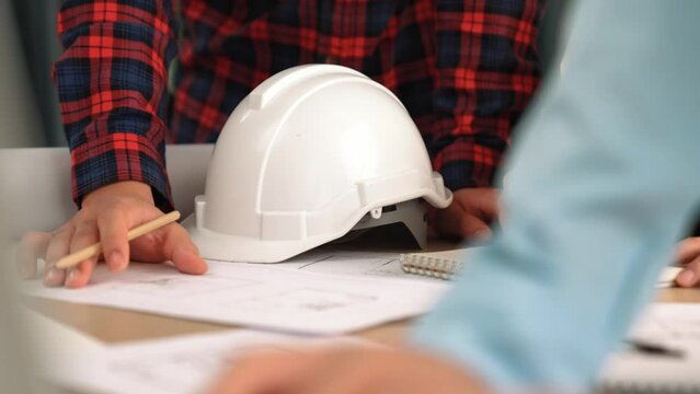Architect and safety engineer discussion about building blueprint displaying on laptop on table with architectural document and wooden block scatter around at modern office. Closeup. Delineation.