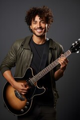 He is a young Hispanic guitarist, wearing a leather jumper and smiling brightly.