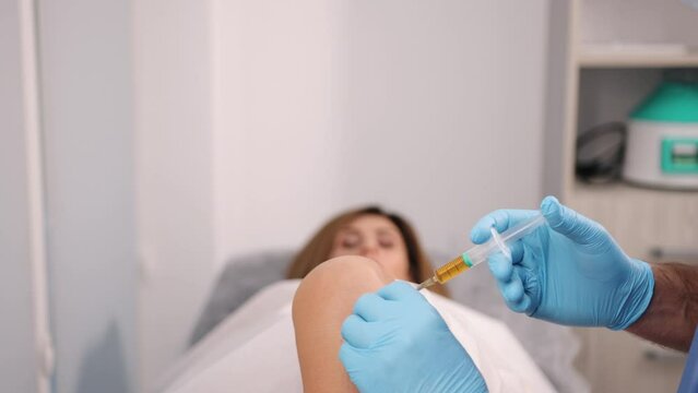 Blue Scrubs, Knee Healthcare, Clinical Treatment. Female patient receives knee injection from surgeon wearing blue scrubs, conducted with careful precision.