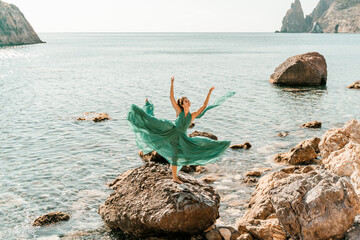 Woman green dress sea. Female dancer in a long mint dress posing on a beach with rocks on sunny...
