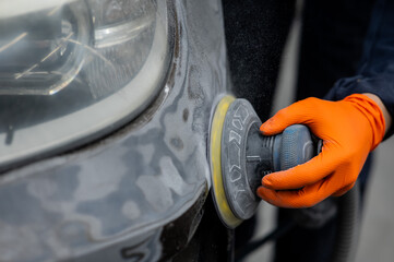 A mechanic sands the putty on a car body with a machine. Repair after an accident. 