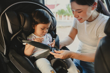 mother is fastening safety belt to toddler girl in car seat, safety baby chair travelling