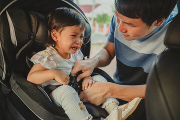 father is fastening safety belt to crying toddler girl in car seat, safety baby chair travelling