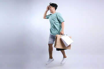 Full Length Of Young Asian Man Looking For Discount While Holding Shopping Bags Isolated On White Background