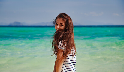 Beautiful happy smiling wonan in casual t-shirt with long brown hair looking on sunny sea and blue...
