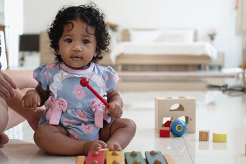 African baby girl  with curly hair holding children's xylophone stick, looking at camera on floor