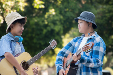 Asian boys holding acoustic guitars, walking a long the road in their community park in the...