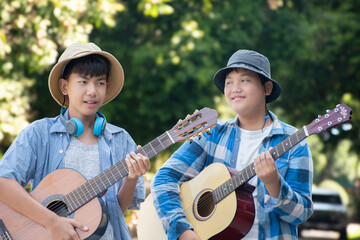 Asian boys holding acoustic guitars, walking a long the road in their community park in the afternoon and playing them together during their summer holiday, recreational activity of children conept.