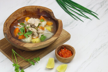 Chicken vegetables soup, Indonesian popular chicken soup made with chicken meat, carrot, potato, cabbage and served with sambal and lime slice. White marble background and copy space.