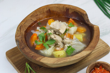Chicken vegetables soup, Indonesian popular chicken soup made with chicken meat, carrot, potato, cabbage and served with sambal and lime slice. White marble background and copy space.