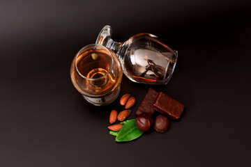 Two glasses of cognac on a black background, next to an almond, mint leaves and chocolates.