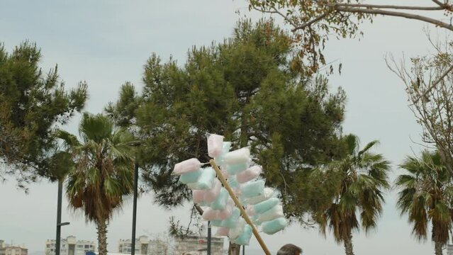 A cotton candy vendor in a resort town walks among palm trees. Cotton candy on a stick.