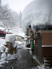 Beautiful Japanese rural winter  scenery, small village street with traditional houses, big snowdrifts on the roof, pine forest in snow on the hill, Ginzan onsen, nature of Yamagata, Japan