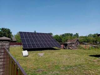 Panels for generating electricity from solar energy are mounted behind a high fence in the yard. Solar panels and generation of energy from renewable sources.