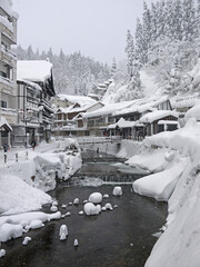 Beautiful Japanese winter scenery, small village with traditional houses, river, pine forest in snow on the hill, Ginzan onsen, nature of Yamagata, Japan