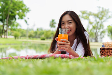 Asian Women picnic in green park smilng face hands holding glass of orange juice fresh fruit cool...