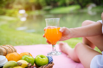 Close up Women picnic in green park hands holding glass of orange juice fresh fruit cool summer....